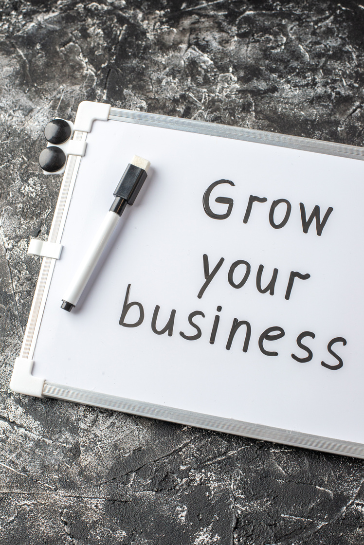 Half Shot of Grow Your Business Writing on White Desk and Marker on Black White Distressed Table